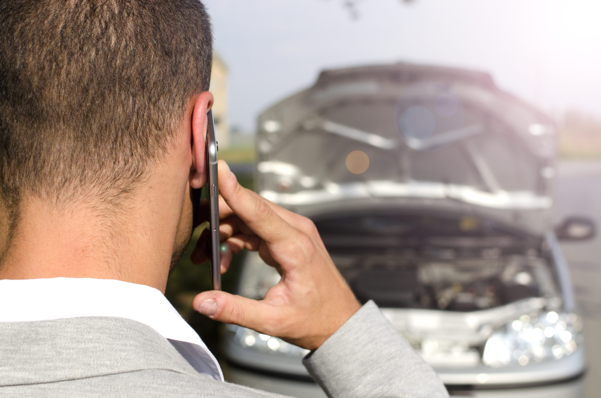 man standing by the broken vehicle calling tow service.